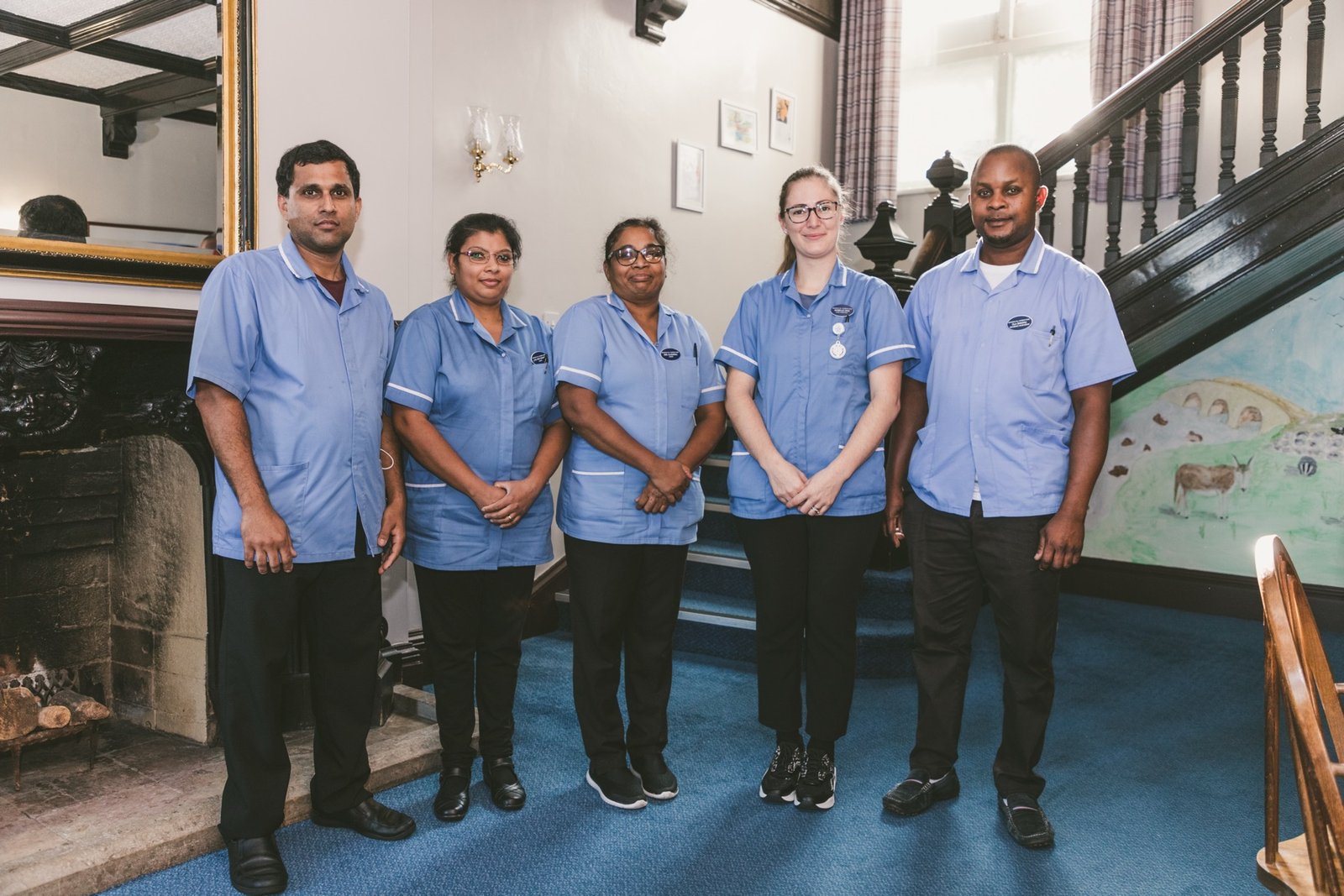 Five care home staff members smiling together by a staircase