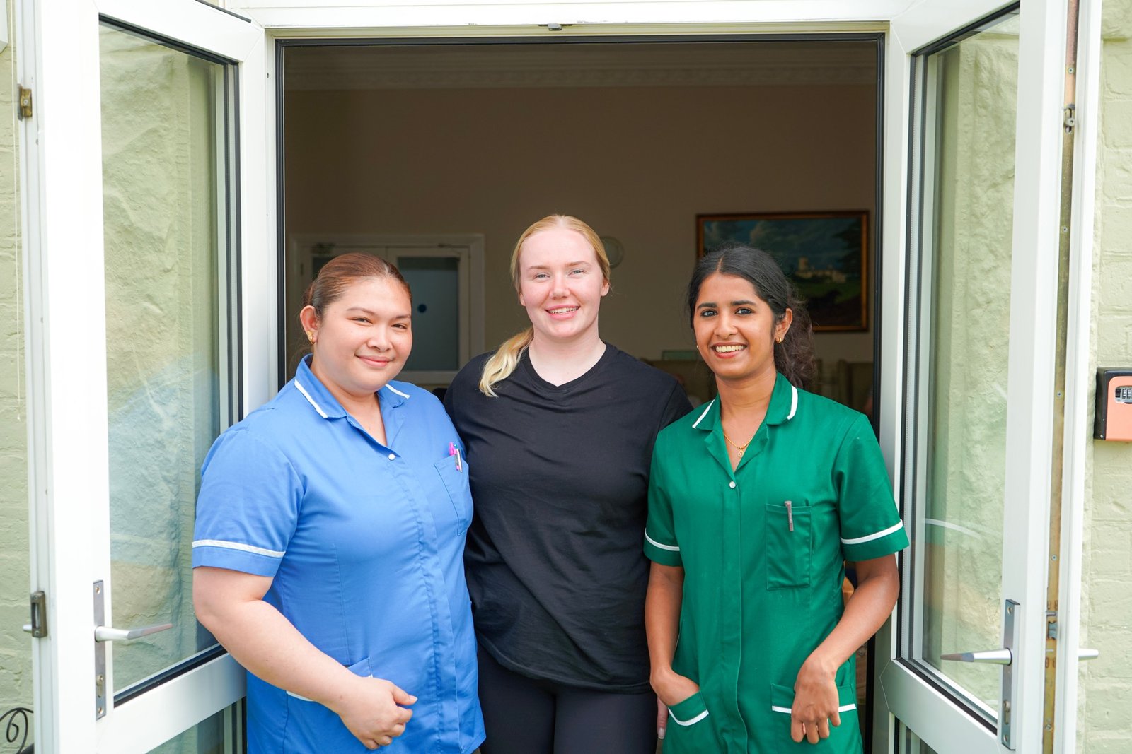 Three care home staff members smiling together at the doorway